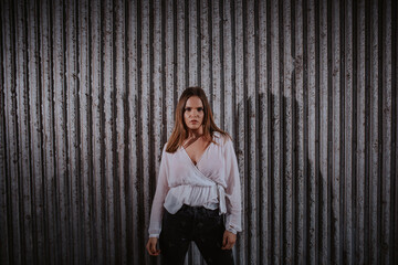 A beautiful young caucasian girl in a white shirt stands in front of a ribbed wall