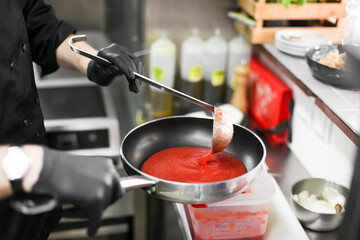 A process of cooking tomato sauce on a restaurant kitchen, mixing red sauce on a pan with a ladle