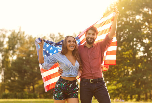Happy couple with america flag celebrating independence day at sunset.