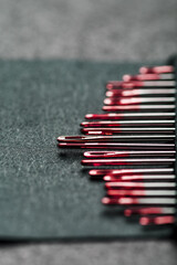 Sewing needles of different sizes in a set of red on a black background.