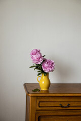 Pink Peony standing in a yellow jug on dark brown oak tabletop