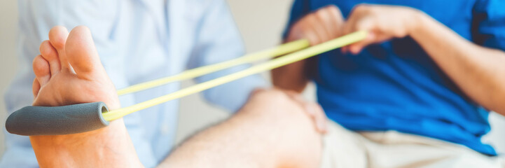 Physiotherapist man giving resistance band exercise treatment About knee of athlete male patient Physical therapy concept