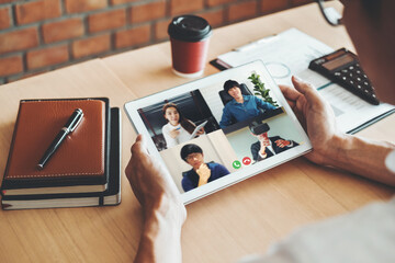 Fototapeta na wymiar Asian man working from home use Smart working and video conference online meeting with Asian team using laptop and tablet online in video call for new projects