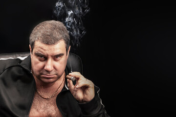 a stern adult man Smoking a cigar looks confidently at the camera. copy space on a black...