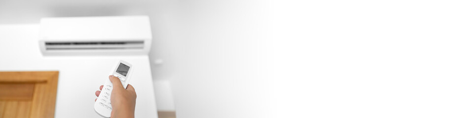 Flat air conditioner on white wall in room interior. Man pushing button on remote