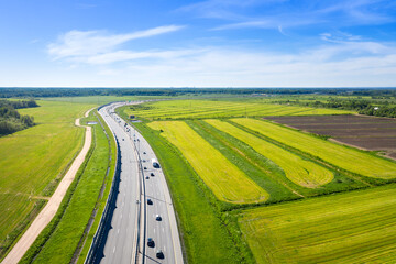 Asphalt Speedway with cars through green field near forest