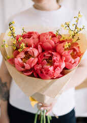 Very nice young woman holding huge beautiful blossoming bouquet of fresh yellow Forsythia and coral Peonies