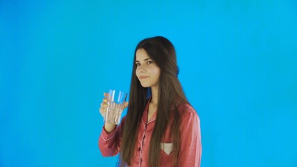 Caucasian teen female girl drinking glass of water. Young woman drinking water from glass on blue background in studio