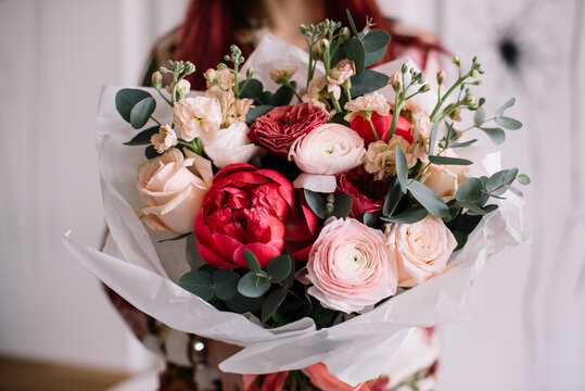 Very nice young woman holding big and beautiful bouquet of fresh ranunculus, roses, peony, eucalyptus, carnations in pink red and white colors, cropped photo, bouquet close up