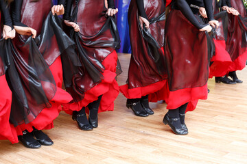 a row of dancing female feet in black shoes and red dresses