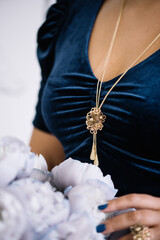 Elegant woman in a blue velvet dress showing jewellery with  blue peonies on the background