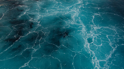 Close-up view of turquoise blue sea or ocean waves creating a marble effect with white flowing lines and blue marine, navy tones visible in the crystal clear water, natural background with copy space