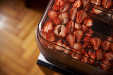 Chopped pieces of strawberries, prepared for drying, lying on white table in kitchen. Fruit dryer machine in process of making delicious snacks. Home dried berries' production. Summertime crop.
