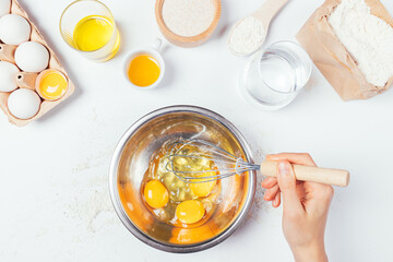 Female hand holding whisk mixes eggs in metal bowl