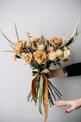 Very nice young woman holding big beautiful blossoming bouquet of fresh roses, carnations, eucalyptus flowers in brown caramel colors on the grey wall background 