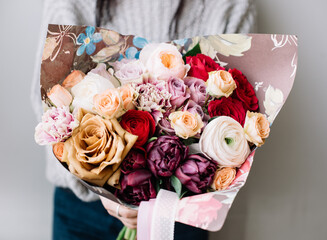 Very nice young woman holding beautiful blossoming bouquet of roses, ranunculus, carnations, tulips flowers cream pink and brown in colors on the grey background