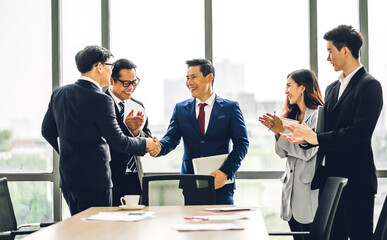 Image two asian business partners in elegant suit successful handshake together in front of group of casual business clapping hands in modern office.Partnership approval and thanks gesture concept