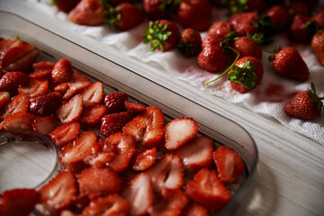 Chopped pieces of strawberries, prepared for drying, lying on white table in kitchen. Fruit dryer machine in process of making delicious snacks. Home dried berries' production. Summertime crop.
