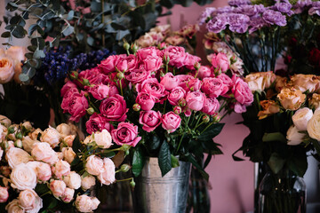 Fresh delivery at the florist shop: vases with blossoming roses, eucalyptus, carnations, ranunculus flowers 