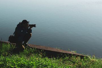 Obraz premium Young male photographer holding a camera in his hands near the river. Landscape photography. With a copy space.