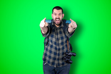 Young traveler man pointing and looking at copy space. Handsome young businessman isolated on green background