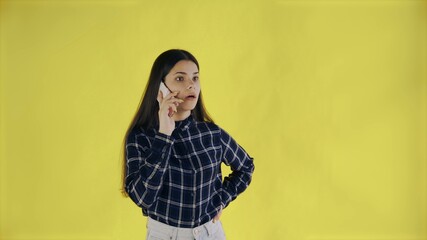 Surprised woman standing isolated over yellow background while talking by phone