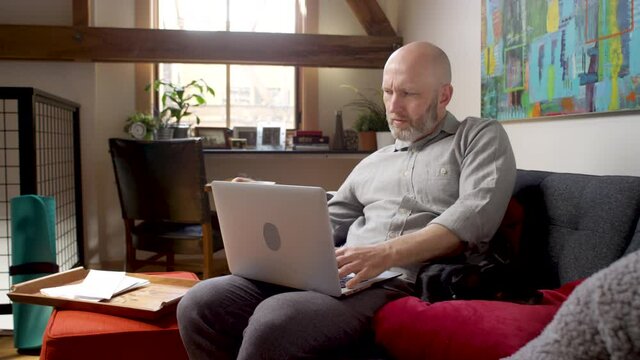 A man working from home takes a sip of tea while working on his laptop