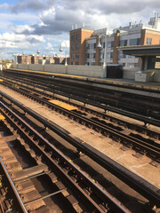 Overground train tracks at an empty subway platform in Queens, NY. Empty subway platform.  Outdoor subway station stop in New York City.  Vacant city. Apartment buildings in the background.