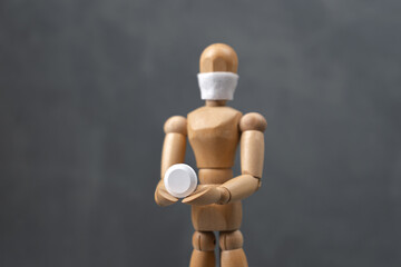 A wooden man in a surgical mask holds a tablet in his hand.