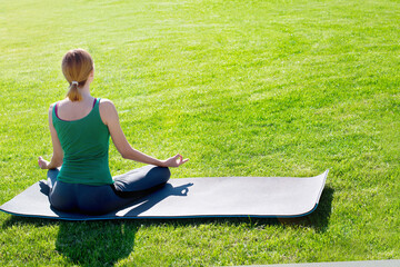 A woman practices yoga outdoors on the grass. Copy space