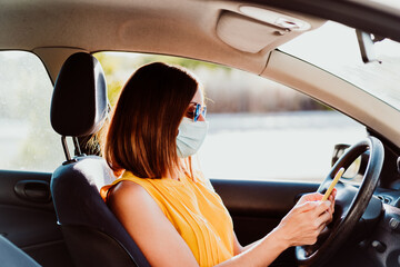 Fototapeta na wymiar young woman in a car using mobile phone, wearing protective mask. Summer season. prevention corona virus concept
