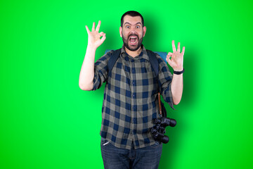 Fototapeta premium Portrait of a cheerful young traveler man showing okay and victory gesture isolated on the chroma background