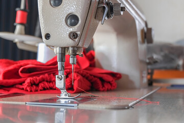 Steel needle presser foot of white industrial sewing machine for sew cloth or fabric with red thread roll close-up.