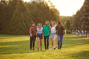 A group of friends have fun walking on the grass in the summer park.
