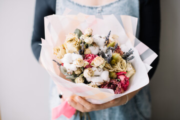 Very nice young woman holding beautiful  bouquet of dry roses, lavender, cotton flowers in white purple and magenta colors on the grey background