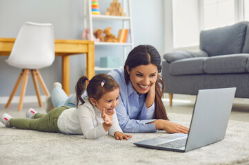 Mom with her daughter watching cartoons or entertainment video online at home. Parent and child with laptop on floor