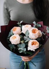 Very nice young woman holding huge beautiful blossoming mono bouquet of fresh David Austin roses in tender pink colors and eucalyptus on the grey background