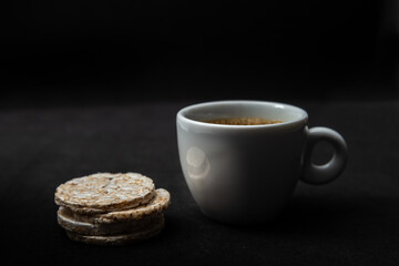 Xícara branca com café e bolachas de arroz sobre a mesa. 