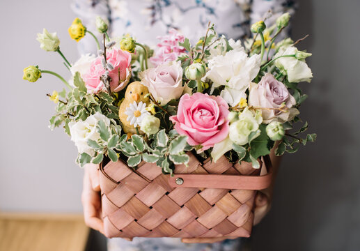 Very nice young woman holding beautiful blossoming easter themed box of fresh roses, eustoma flowers in white and pink colors on the grey background 