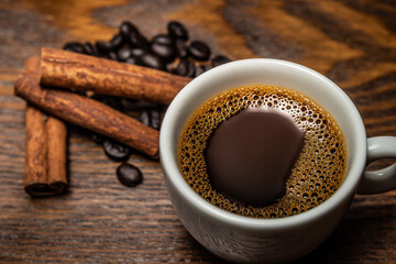 Xícara de café, pau de canela e grãos de café sobre a mesa.