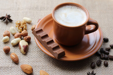 Cup of coffee with chocolate, cinnamon and nuts on the sackcloth