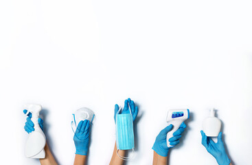 Raised hands in medical gloves holding masks, sanitizers, soap, non contact thermometer on white...