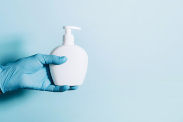 Hands in gloves holding soap bottle and medical face mask on blue background. Copy space....