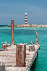 Old wooden pier with seagulls and red and white lighthouse at Cancun, Caribbean sea, Mexico. Vertical Screen Orientation