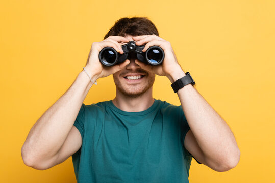 cheerful man looking through binoculars on yellow