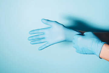 Woman doctor wears medical gloves over blue background. Copy space. National Doctors' Day. International Nurses Day. Health protection equipment during quarantine Coronavirus pandemic