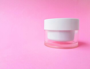 Transparent jar with cream and white lid on a bright pink background. Space for text.