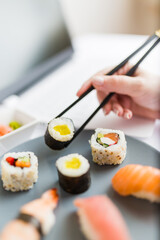 Asian sushi set with laptop and female hand holding chopsticks. Healthy meal at work food delivery concept.