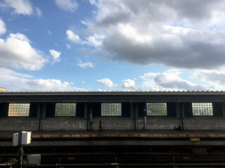 Empty overground subway platform with subway tracks in foreground. Blue sky and puffy clouds at vacant New York City train station, empty city, decline in public transport due to COVID-19.
