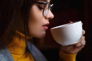 Beautiful dreamy girl in stylish sharp glasses. With a cup in his hands.